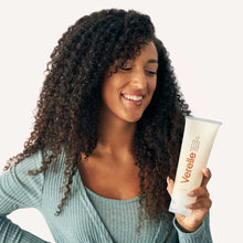 Load image into Gallery viewer, Woman with long defined curly hair holding Verelle all in one milky cream in her hand