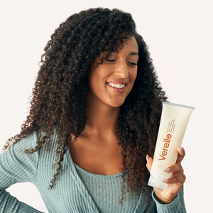Woman with long defined curly hair holding Verelle all in one milky cream in her hand